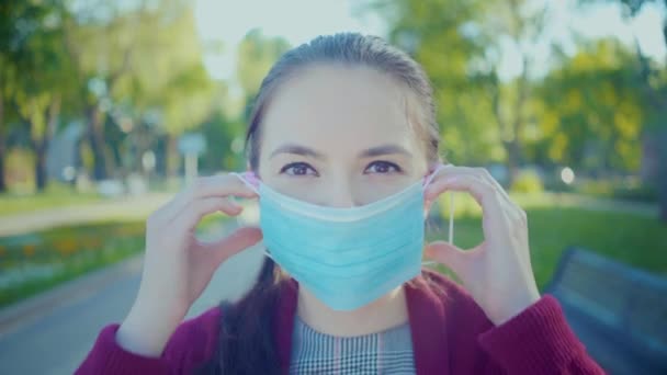 Hezká dívka uvedení na lékařské masky pro coronavirus covid-19 ochrany venku. — Stock video