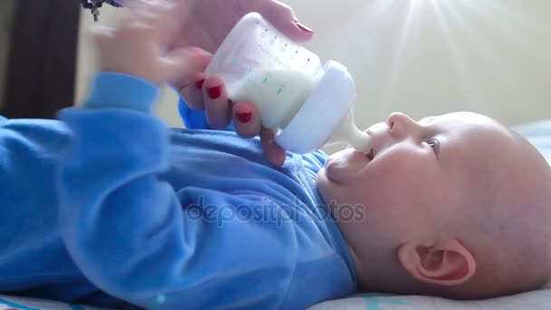 Bambino bambino che piange quando ottenere bottiglia con latte infantile dalle sue mani madri a letto. Nutrizione infantile sana. Soleggiato al coperto — Video Stock