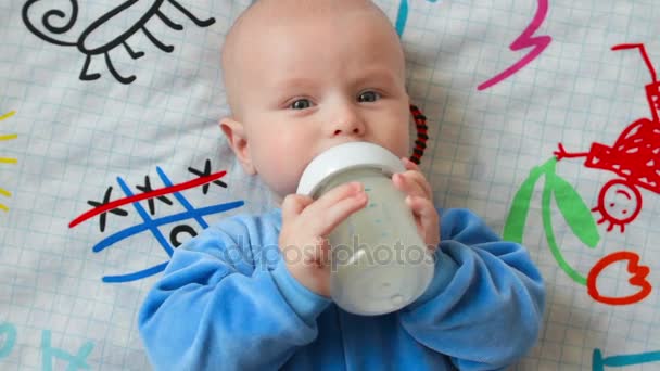 La madre le da al bebé un biberón de leche. Come sosteniendo una botella en su mano, y luego la pierde. Él está tratando de nuevo de tomar una botella en las manos — Vídeo de stock