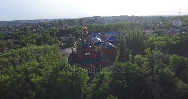 Aerial view of the red Orthodox Church with golden domes. Red-stone church from helicopter. The church is surrounded by a green forest. Church with golden domes and crosses. Russia, October 2016 — Stock Video