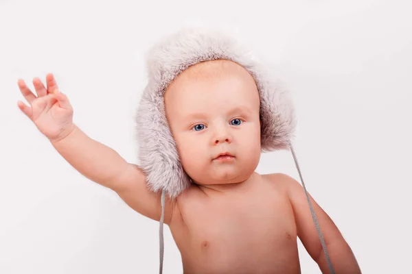 Retrato de bebê caucasiano bonito nove meses de idade com olhos azuis usando um chapéu peludo em um fundo leve segurando a mão Imagens Royalty-Free