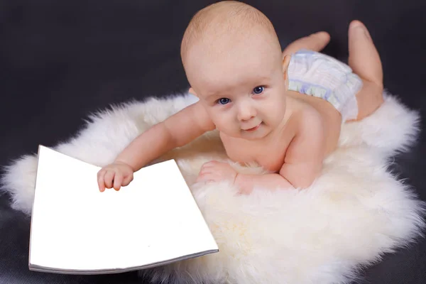 Hermoso bebé con la revista en sus manos que pone en la piel. Mirando a la cámara y sonriendo —  Fotos de Stock