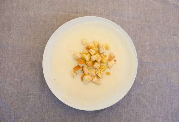 Tasty cream soup with toast on white plate and grey linen background served in a cafe top view — Stock Photo, Image