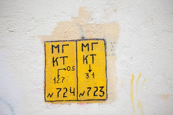 Yellow square technical mark on the wall with numbers and cyrillic letters (abbreviations MG and KT)
