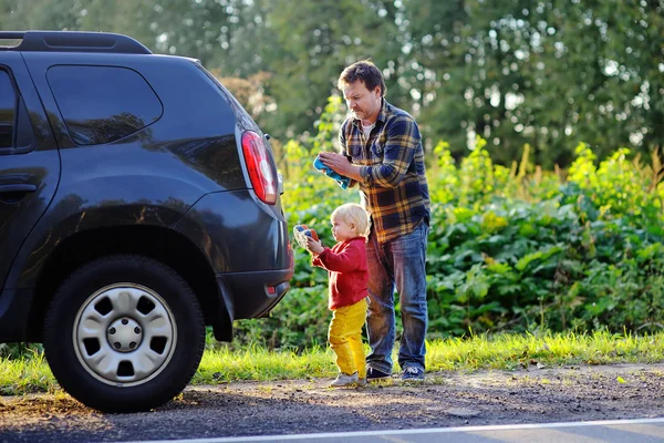 Father with his toddler son washing car together