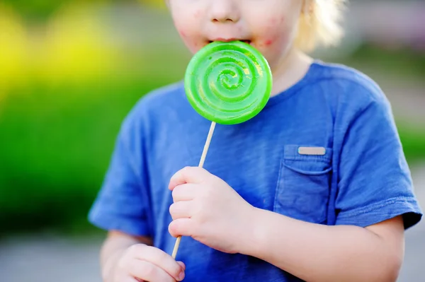 Criança com reação alérgica comer grande pirulito verde — Fotografia de Stock