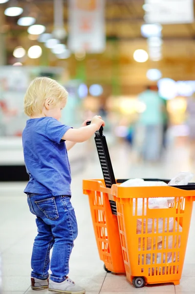 Kleuter jongen met winkelwagentje in de supermarkt — Stockfoto