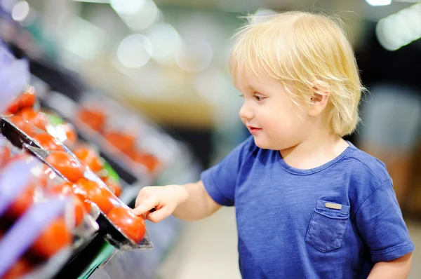 Niño pequeño en una tienda de alimentos o en un supermercado eligiendo tomates frescos —  Fotos de Stock