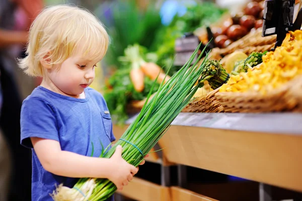 Schattig peuter jongen in een food winkel kiezen verse biologische groene ui — Stockfoto