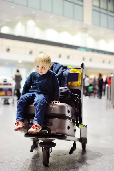 Moe jongetje zittend op koffers op de luchthaven — Stockfoto