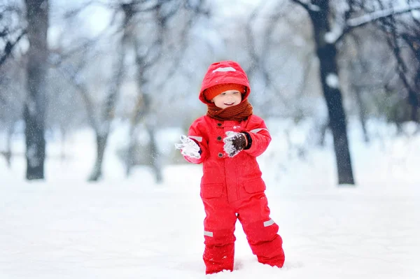Портрет маленького смешного мальчика в красной зимней одежде, веселящегося со снегом во время снегопада — стоковое фото