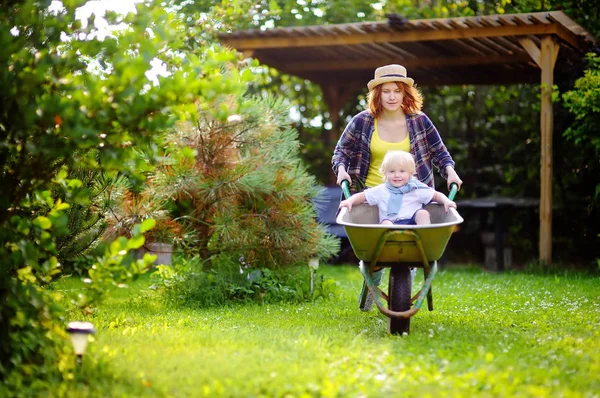 Bedårande barn pojke ha roligt i en skottkärra som driver av mamma — Stockfoto