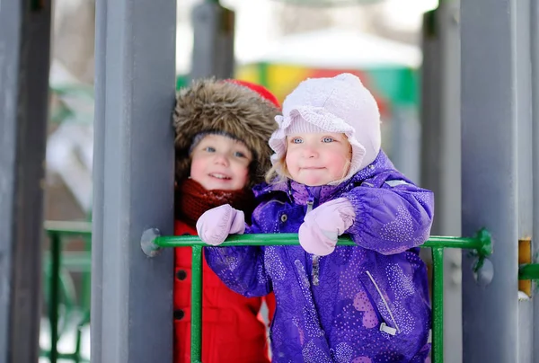 Niños pequeños en ropa de invierno divirtiéndose en el patio de recreo en el día de invierno nevado — Foto de Stock