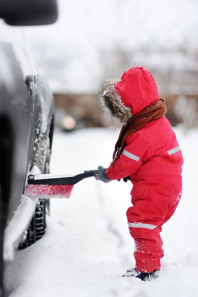 Criança pequena bonito ajudando a escovar uma neve de um carro — Fotografia de Stock