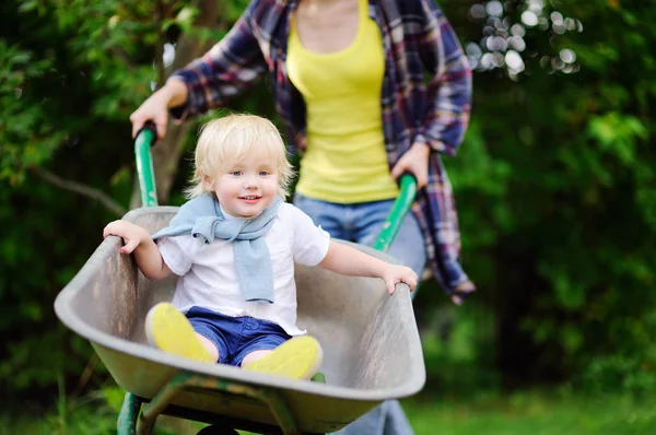 可爱的幼儿男孩用独轮车推的妈妈在国内的花园里玩 — 图库照片