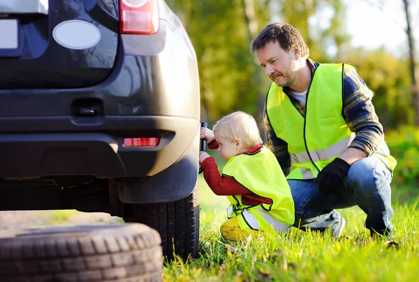 Ayah dan anaknya memperbaiki mobil dan mengganti roda bersama-sama pada hari musim panas — Stok Foto