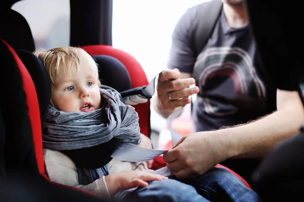 Middle age father helps his toddler son to fasten belt on car seat — Stock Photo, Image