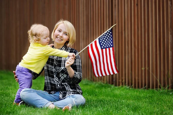 Щаслива молода жінка зі своєю маленькою дівчинкою тримає американський прапор — стокове фото