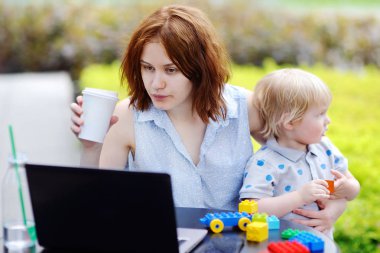 Young mother working oh laptop and holding her son clipart