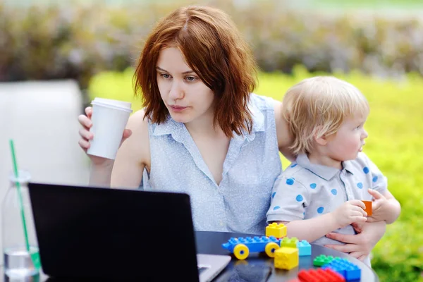 Jovem mãe trabalhando oh laptop e segurando seu filho — Fotografia de Stock