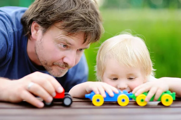 Отец средних лет со своим маленьким сыном, играющим с игрушечными поездами на открытом воздухе — стоковое фото