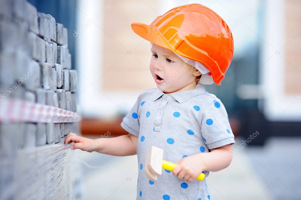 Little builder in hardhats with hammer working outdoors