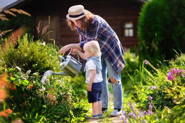 Batole chlapec a jeho mladá matka zalévání rostlin v zahradě — Stock fotografie