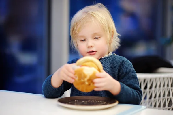 Lindo chico rubio comer hamburguesa en restaurante de comida rápida —  Fotos de Stock