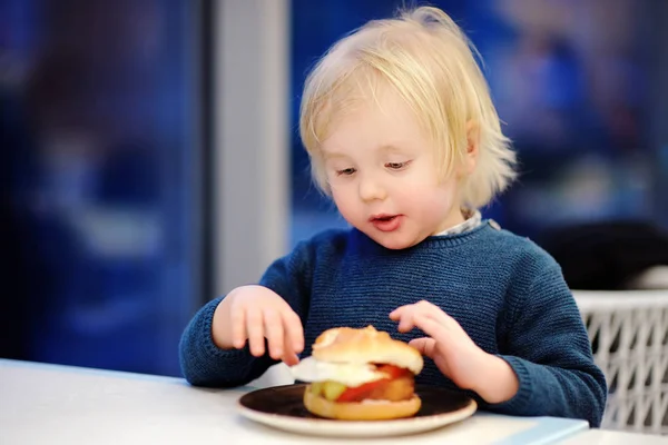 Roztomilý blonďák jíst hamburger v restauraci rychlého občerstvení — Stock fotografie