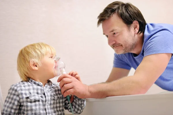 Middle age father helping his toddler son with inhalation therapy by the mask of inhaler — Stock Photo, Image
