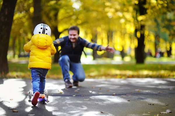 Батько середнього віку показує своєму маленькому синові, як їздити на скутері в осінньому парку — стокове фото