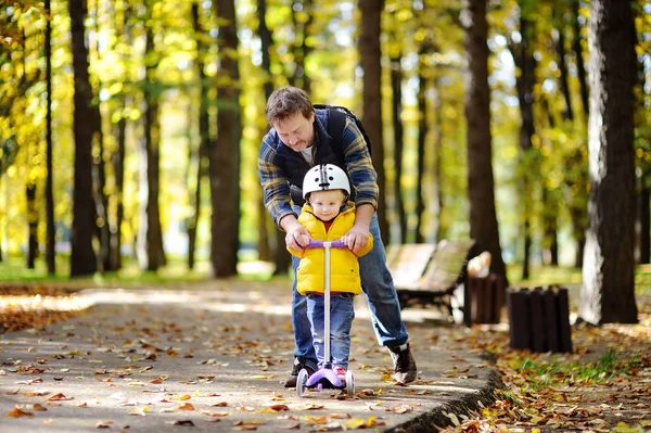 Padre de mediana edad mostrando a su hijo pequeño cómo montar un scooter en un parque de otoño —  Fotos de Stock