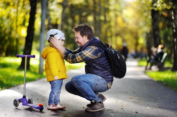 Vater mittleren Alters hilft seinem kleinen Sohn, seinen Helm aufzusetzen — Stockfoto