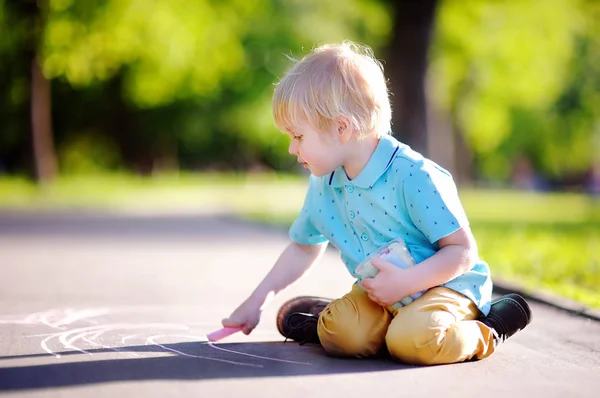 Niño concentrado sentado y dibujando con tiza de color sobre asfalto — Foto de Stock
