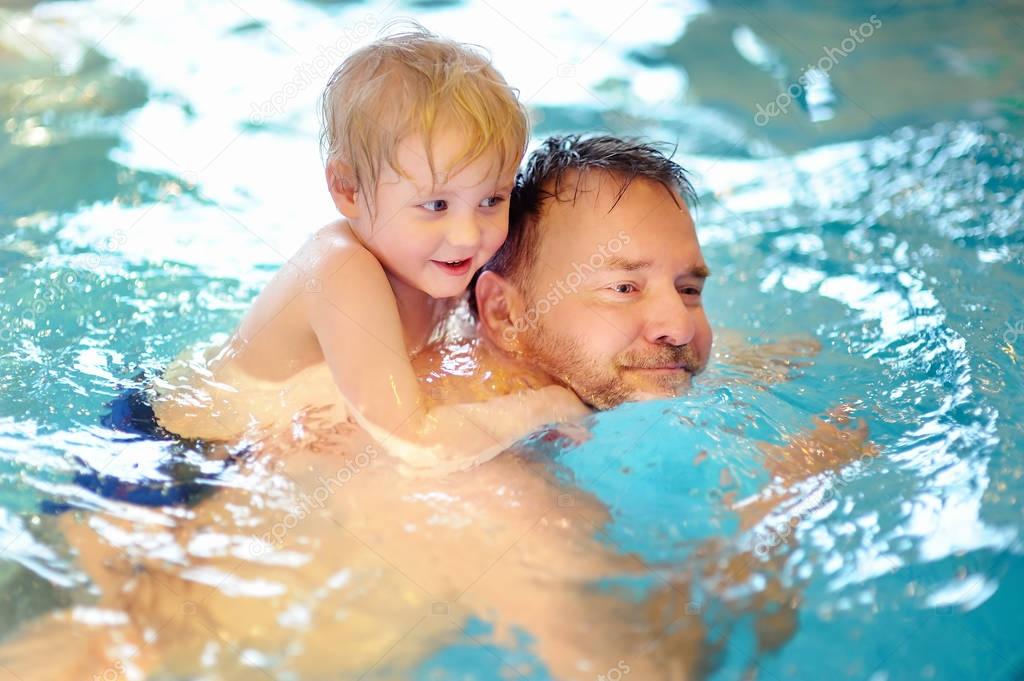 Happy smiling little boy with his father in swimming pool
