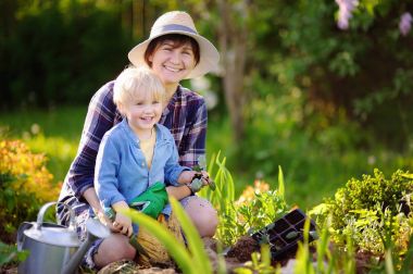 Güzel orta yaş kadın ve sevimli torunu yaz gününde iç bahçesinde yatakta fidan dikim