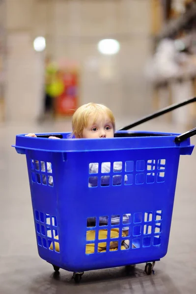 Carino bambino seduto / nascosto nel carrello della spesa in plastica in un moderno negozio di mobili per la casa — Foto Stock