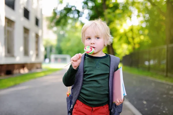 Söt liten skolpojke med sin ryggsäck och lollipop. Tillbaka till skolan-konceptet. — Stockfoto