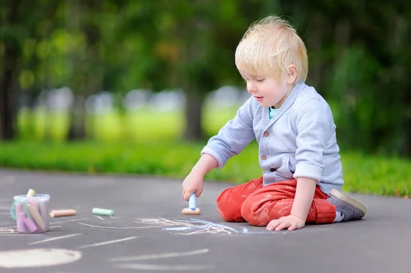 Glad liten unge pojke ritar med färgad krita på asfalt. — Stockfoto