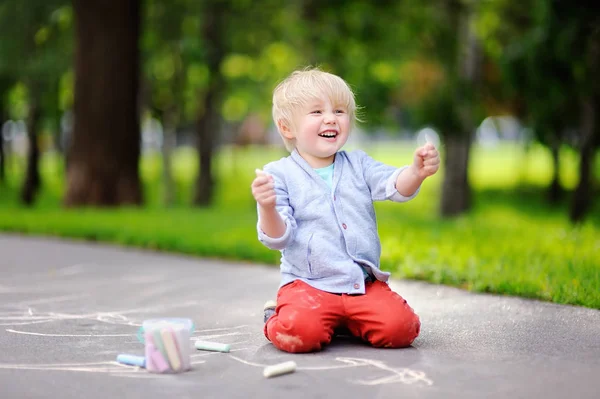 Feliz niño pequeño dibujo con tiza de color sobre asfalto . — Foto de Stock