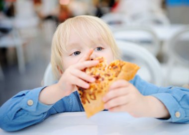 Sevimli sarışın çocuk dilim pizza fast food restoranında yemek