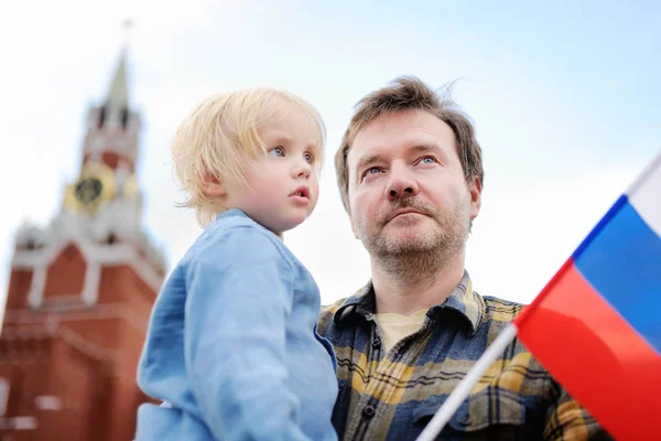 Homem de meia-idade e seu filho com bandeira russa com torre Spasskaya (Rússia, Moscou) em segundo plano — Fotografia de Stock