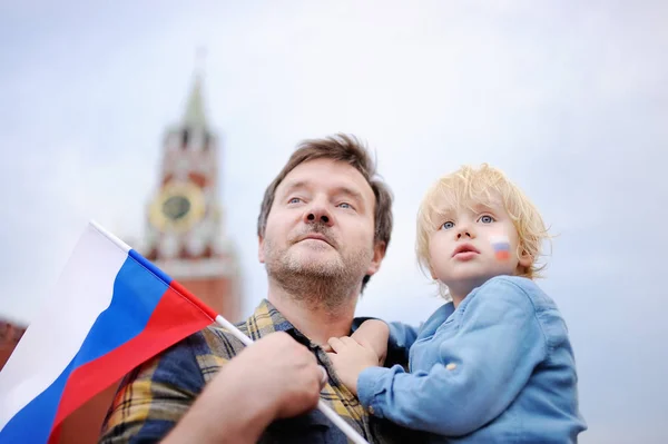 Muž středního věku a jeho malý syn s ruskou vlajkou s Spasská věž (Rusko, Moskva) na pozadí — Stock fotografie
