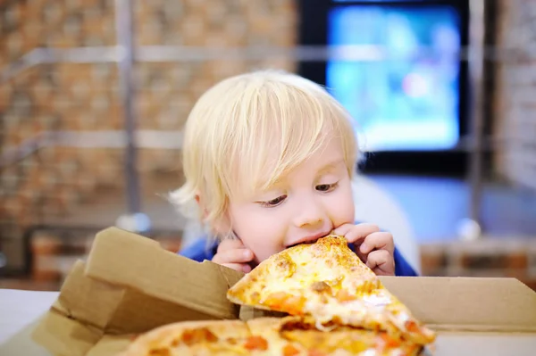 Lindo chico rubio comiendo rebanada de pizza en restaurante de comida rápida —  Fotos de Stock