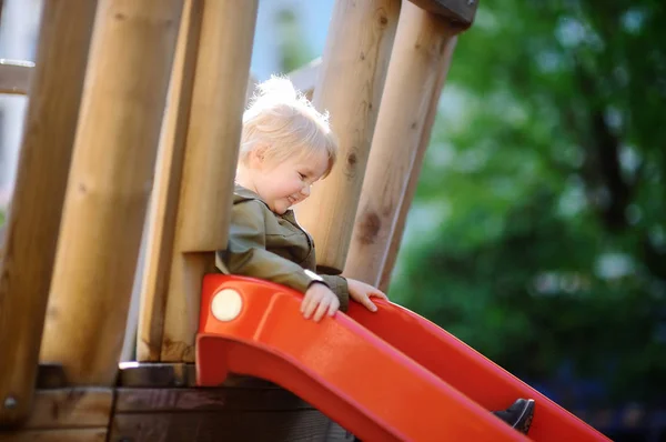 Joyeux petit garçon qui s'amuse sur une aire de jeux extérieure / sur une glissière — Photo