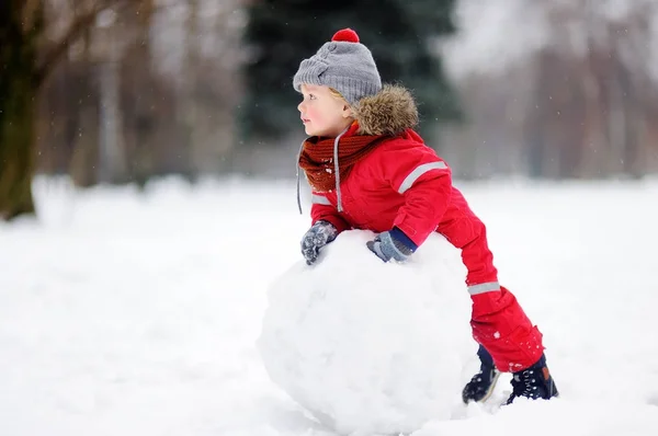 Menino em roupas vermelhas de inverno se divertindo com boneco de neve — Fotografia de Stock