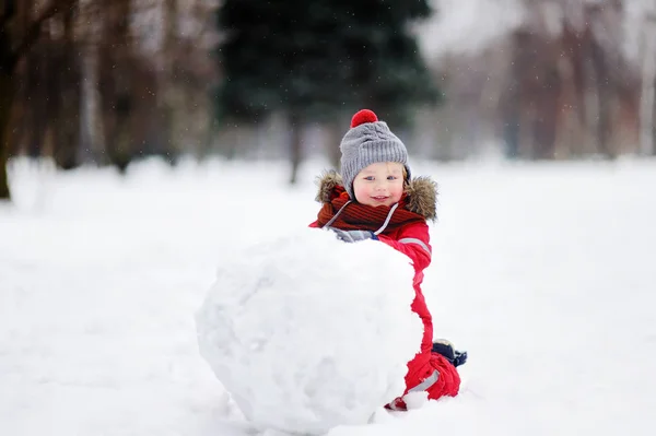 Menino em roupas vermelhas de inverno se divertindo com boneco de neve — Fotografia de Stock
