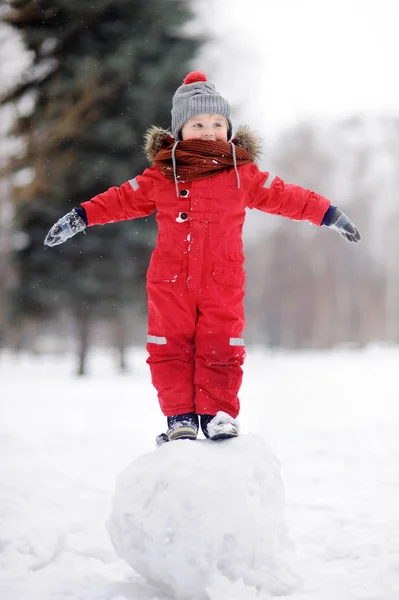 Menino em roupas vermelhas de inverno se divertindo com boneco de neve — Fotografia de Stock