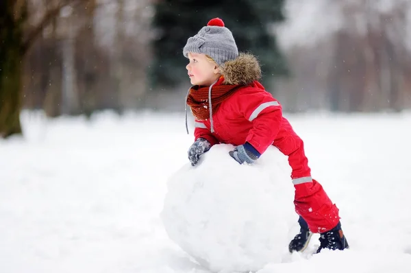 Kardan adam ile eğleniyor kırmızı kış giysileri içinde küçük çocuk — Stok fotoğraf