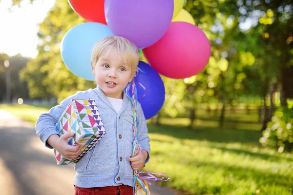 Mignon garçon tenant paquet de ballons colorés et cadeau dans une boîte de fête. Joyeux anniversaire ! — Photo